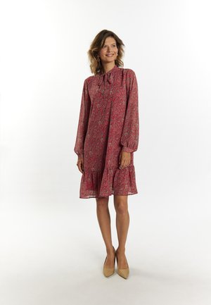 Rode jurk met een patroon, lange mouwen, een strikdecolleté en een rimpelige onderrand. Gecombineerd met beige puntige hakken. Glad stofoppervlak.