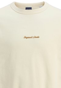 Kremowy bawełnowy sweatshirt z prążkowanym okrągłym dekoltem. Zawiera haft "Originals Studio" w kolorze brązowym. Prosta, gładka tekstura.