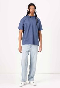 Blå bomulls t-skjorte med en avslappet passform, kort ermer, rund hals, kombinert med lyseblå rettbente jeans og hvite sneakers.