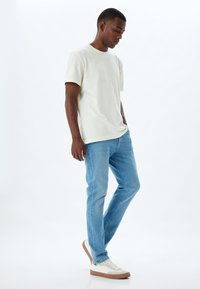 Camiseta de algodón de color claro combinada con pantalones vaqueros de mezclilla azules. Las zapatillas tienen una parte superior blanca y una suela marrón claro. Diseño simple y moderno.