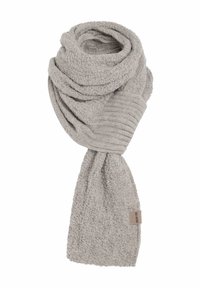 Gehaakte sjaal van zacht lichtgrijs materiaal. Heeft een ribbelstructuur en een label met de merknaam. De textuur geeft een interessant visueel effect.