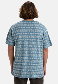 Light blue short-sleeve shirt featuring a white leaf and geometric pattern, made from soft fabric with a relaxed fit and crew neckline.