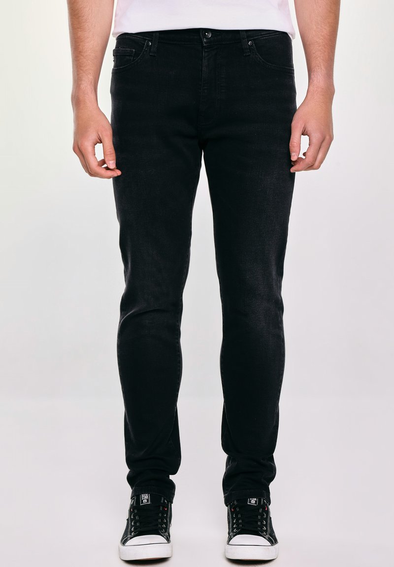 Czarne dżinsy slim-fit wykonane z denimu, z pięcioma kieszeniami, z zapięciem na guzik oraz delikatnym przetarciem dla nadania tekstury. Noszone z czarnymi trampkami.