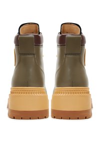 Botas de tobillo de cuero verde oliva con un acento marrón, que cuentan con una suela gruesa y texturizada, forma redondeada y tiradores en la parte trasera.