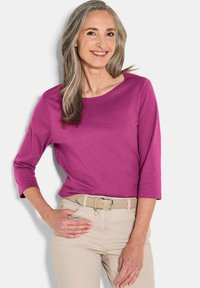 Magenta langmouwen top met een ronde hals, gecombineerd met beige broek en een lichtgekleurde riem. Soepele textuur, casual pasvorm.