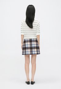 Kortærmet stribet top i hvid med røde og blå detaljer, parret med en brun ternet nederdel med blå accenter. Sorte flade sko.