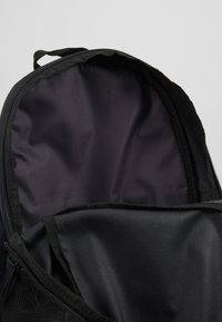 Sac à dos noir avec un dessus arrondi, fermeture éclair et doublure intérieure lisse. Comprend des poches latérales en maille et des coutures renforcées.