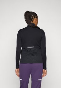 Black long-sleeve top with a high collar, featuring textured back pattern and white accent. Paired with purple pants and minimalistic design.
