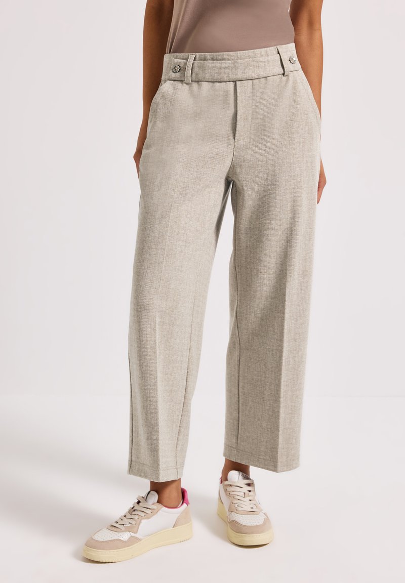 Světle šedé tailored kalhoty s texturovanou tkaninou, širokými nohavicemi, vysokým pasem a předními kapsami, spárované s béžovými a růžovými teniskami.