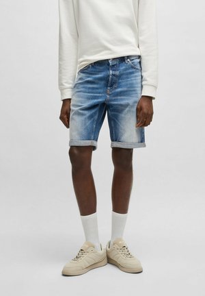 Jeansshorts i ljusblått med en blekt finish, rullade fållar, tillsammans med en krämfärgad långärmad skjorta och beige sneakers.