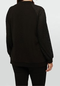 Felpa nera con maniche lunghe in pizzo strutturato con motivo leopardato. Tessuto morbido con vestibilità comoda e polsini a coste.