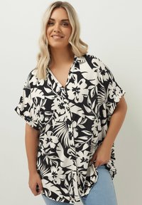 Kortärmad, knappad skjorta i svart och vit blommönster. Har en lös passform, med en krage och sidofickor för ökad rörelsefrihet.