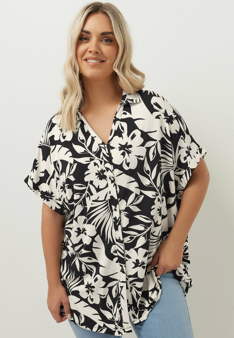 Kortärmad, knappad skjorta i svart och vit blommönster. Har en lös passform, med en krage och sidofickor för ökad rörelsefrihet.