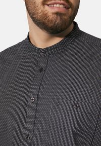 Hemd mit Kragen und Knopfleiste, das ein schwarz-weißes kariertes Muster, eine textile Struktur und eine Brusttasche mit einem subtilen Designdetail aufweist.