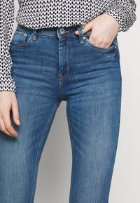 Blå denimjeans med slim fit, med fickor och en subtil orange sömdetalj. I kombination med en blus med svart och vit prick.