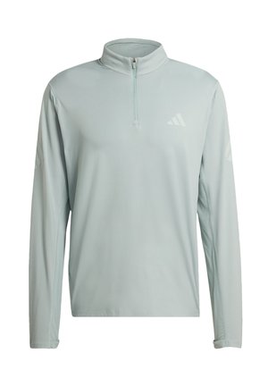 Světlounce šedý atletický pulovr s dlouhým rukávem, čtvrtinovým zipem a jemným logem Adidas na hrudi a rukávech, pohled zepředu.