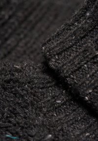 Donkergrijze gebreide stof die gedetailleerde rib- en kabelbrei-texturen toont die nauw met elkaar verweven zijn.