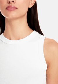 White, ribbed sleeveless top with a round neckline. Smooth texture, fitted design, and clean lines emphasize simplicity.