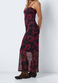 Blumenkleid im Maxiformat mit dünnen Trägern, das ein schwarzes und burgunderfarbenes Muster zeigt. Der untere Abschnitt hat transparente Mesh-Panels. Kombiniert mit braunen Stiefeln.