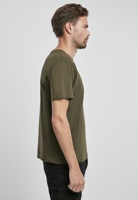 Camiseta de manga corta color verde oliva, hecha de un tejido suave, con cuello redondo y un corte holgado, mostrada de lado sobre un fondo sencillo.