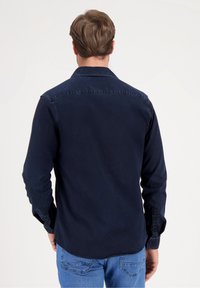 Camisa azul marino de botones hecha de algodón, con cuello clásico, mangas largas y dobladillo curvado. Puños redondeados con botones.