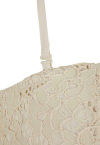 Tissu en dentelle beige à motif floral avec une bride ajustable dotée d'une petite attache sur le bord supérieur.