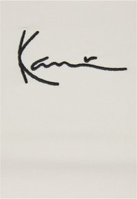 Tissu blanc avec un motif de signature brodé noir bien en vue. La texture est lisse avec un léger relief.