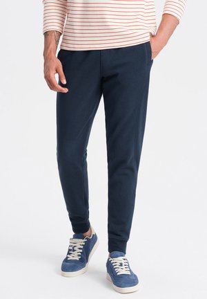 Navy Sweatpants aus weichem Material mit tailliertem Design, elastischen Bündchen und Seitentaschen, kombiniert mit blauen Turnschuhen.