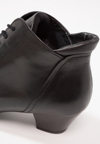 Černý kožený kotník s kulatou špičkou, diskrétními kontrastními švy, hladkým povrchem a nízkým, masivním podpatkem.