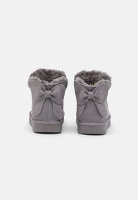 Bottines en daim grises avec doublure en fausse fourrure, présentant des nœuds décoratifs à l'arrière, des côtés texturés et des semelles en caoutchouc plates.
