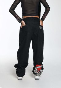 Jeans negros holgados con diseño de calavera y corazón bordado en los puños. Cuenta con bolsillos estándar y una sutil marca en el bolsillo trasero.