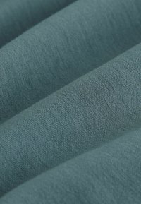 Teal stof in plooien, die een zachte textuur met een subtiel weefpatroon laat zien. Het materiaal lijkt lichtgewicht en glad aan te voelen.