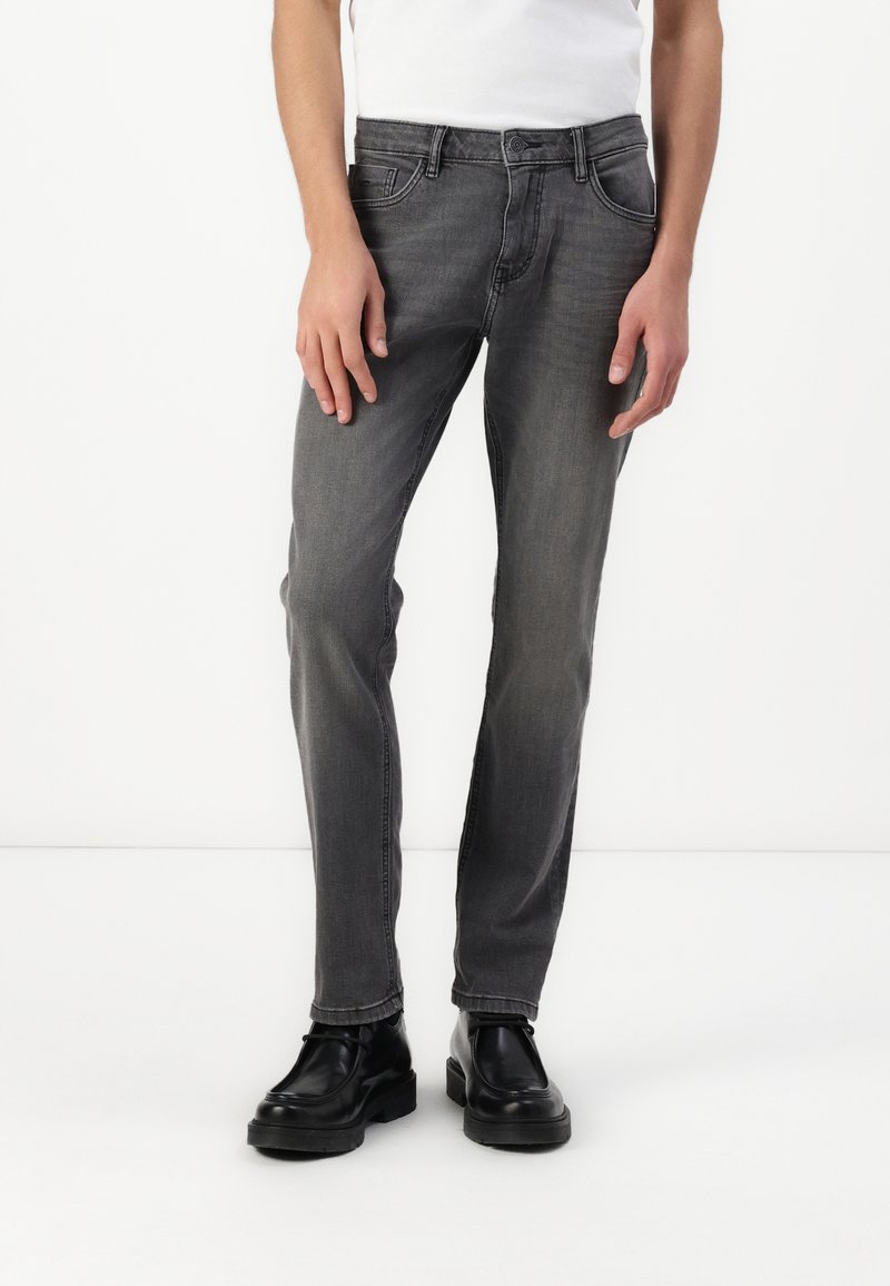 Vaqueros de denim gris con corte ajustado, cinco bolsillos y un ligero desvanecimiento. Combinados con botas negras de cordones. Diseño simple y limpio.