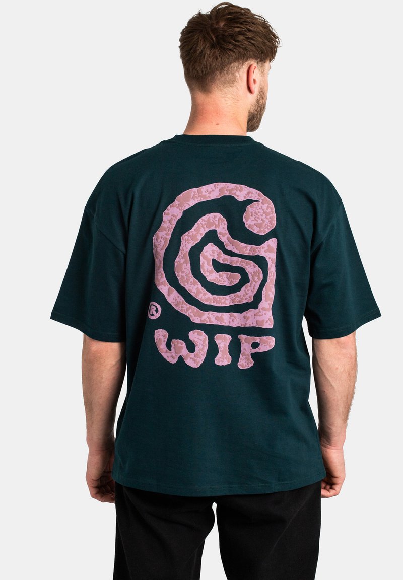 Camiseta de manga corta verde oscuro con un gran logotipo espiral abstracto en rosa y el texto "WIP" en la parte posterior; material de algodón con un corte relajado.