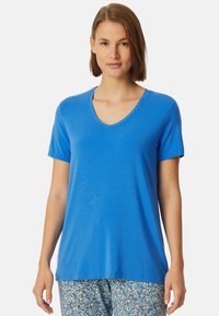 Modrá v-neck tričko vyrobené z hladké l�átky; krátké rukávy, volný střih. V kombinaci se vzorovanými, světlými kalhotami s květinovým vzorem.