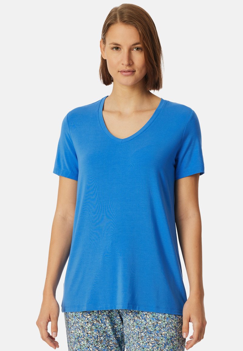 Blå v-ringad t-shirt i ett mjukt tyg; kort ärm, avslappnad passform. Kombinerad med mönstrade, ljusa byxor med blommönster.