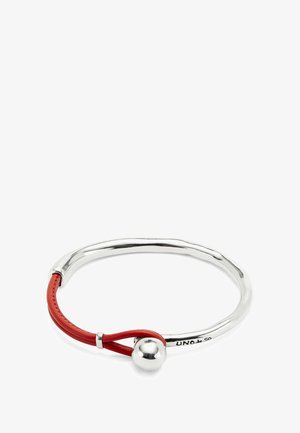 Brazalete de plata con una esfera metálica brillante y un detalle de lazo de cuero rojo, grabado con "UNOde50."