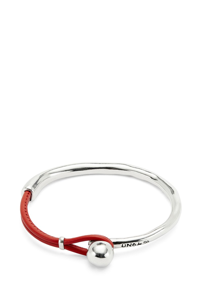 Brazalete de plata con una esfera metálica brillante y un detalle de lazo de cuero rojo, grabado con "UNOde50."