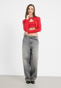 Červený rebrovaný crop top s dlhým rukávom a výrezom v tvare kľúčovej dierky, skombinovaný s vysokými, voľnými sivými riflami a čiernymi lodičkami so špicatou špičkou.