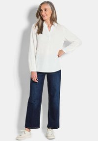 Witte blouse met lange mouwen, een kraag en een knopenlijst aan de voorkant, gecombineerd met donkerblauwe wijde jeans en witte sneakers.