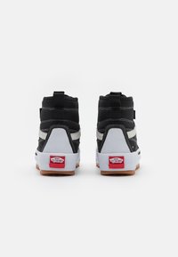 Höga sneakers med svart tyg, vit sidostrand och gummisålar. Röd hällogo och grå detaljer på baksidan och sidorna.