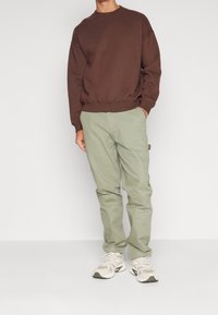 Sudadera de algodón marrón combinada con pantalones verde claro; los zapatos tienen una mezcla de beige y gris con acentos texturizados. Diseño sencillo, corte relajado.