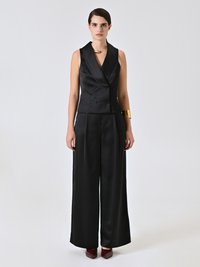 Jumpsuit in satin nero con top a gilet doppiopetto, gambe ampie e colletto tagliente. Accentuato con gioielli dorati e scarpe bordeaux.
