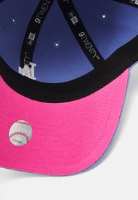 Baseballkappe mit einem pinken Schirm, blauen Krone, schwarzem Innenband und einem runden Aufkleber mit einer Baseballgrafik auf der Unterseite.