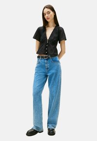 Zwarte korte mouwen blouse met knoopdetails; gecombineerd met lichtblauwe, losse jeans en zwarte chunky schoenen. Glad stof, casual stijl.
