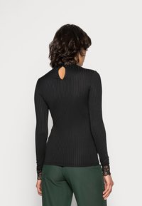 Svart ribbad långärmad topp med hög hals och detalj i form av en nyckelhål baktill. Har spetsdetaljer vid ärmslut. Kombinera med gröna byxor.