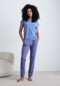 Ljusblå t-shirt med kort ärm med texten "Sov när du drömmer". Lila mönstrade pyjamasbyxor. Mjuk tyg, avslappnad passform.