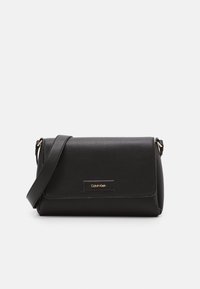 Svart läderväskan i crossbody-modell med texturerad yta, vikbar klaff, guldiga logodetaljer och justerbar axelrem. Kompakt och rektangulär form.