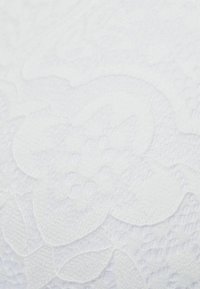 Bílá texturovaná látka s vyraženým květinovým vzorem s různými úrovněmi reliéfu, který dodává hloubku a detail povrchu.