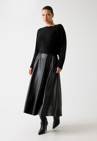 Maglione nero lavorato a maglia con maniche ampie abbinato a una lunga gonna di pelle nera fluente e stivali alti neri con tacco a punta.